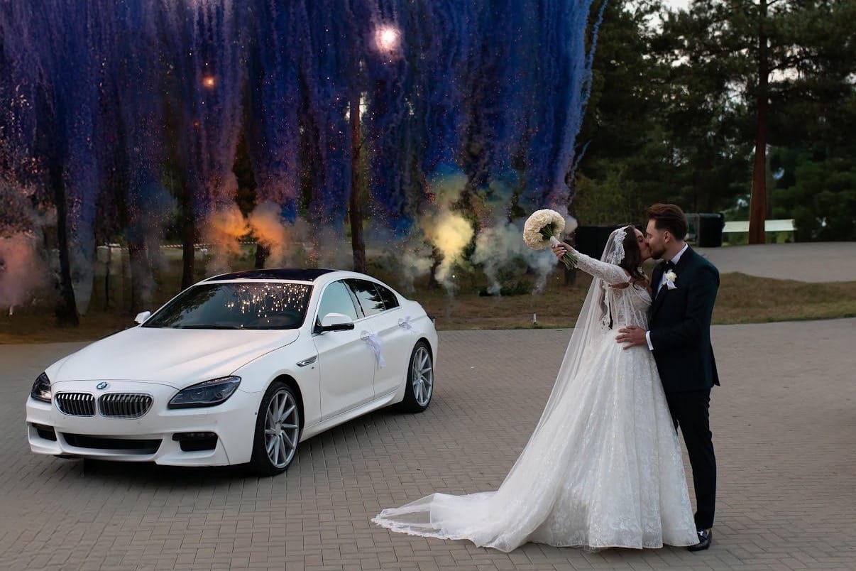 Białe BMW 650i xDrive Gran Coupé udekorowane na ślub, obok Para Młoda i fajerwerki